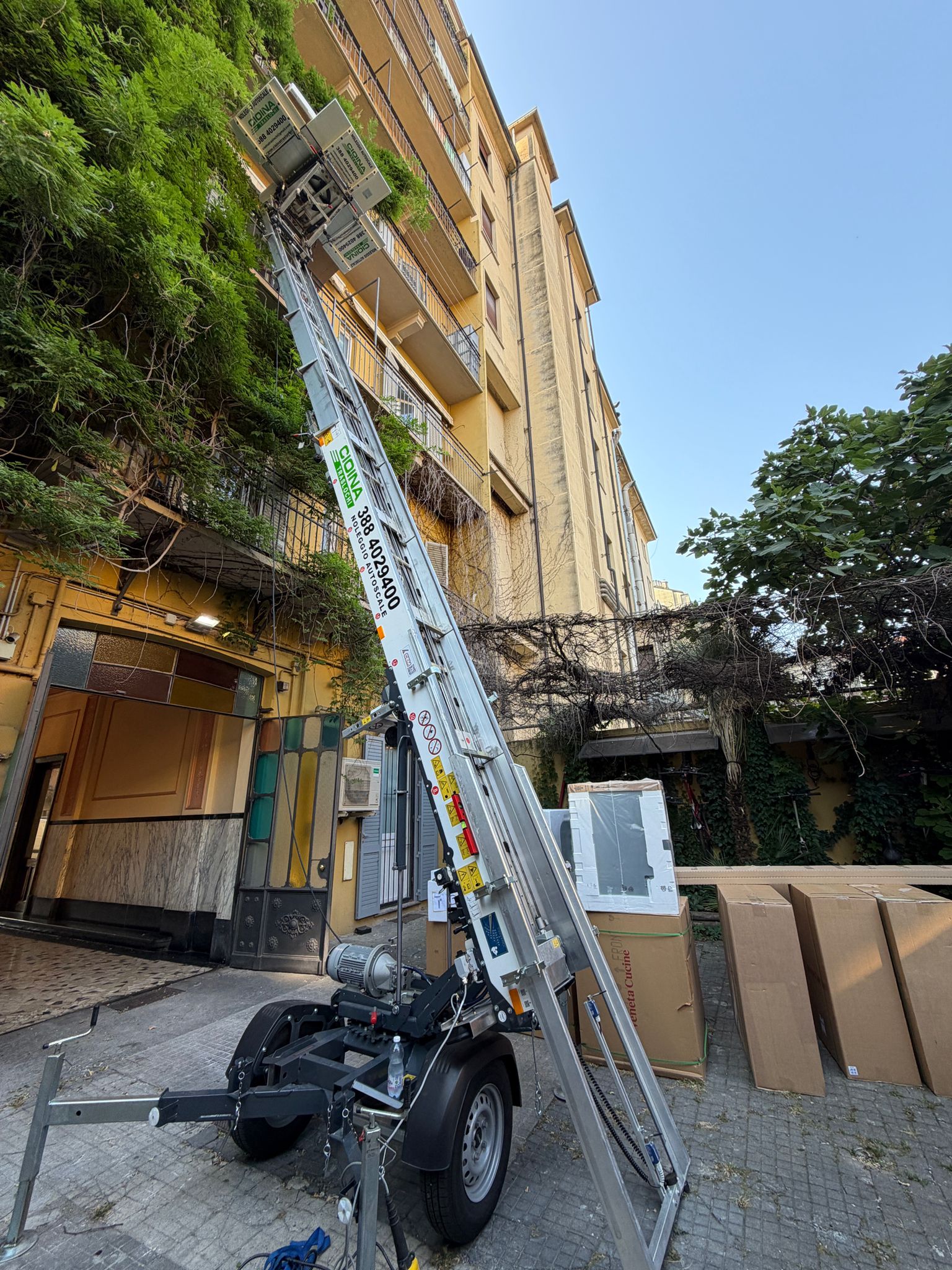 Autoscala carrellata a traino estesa lungo un palazzo, con scatoloni pronti al carico