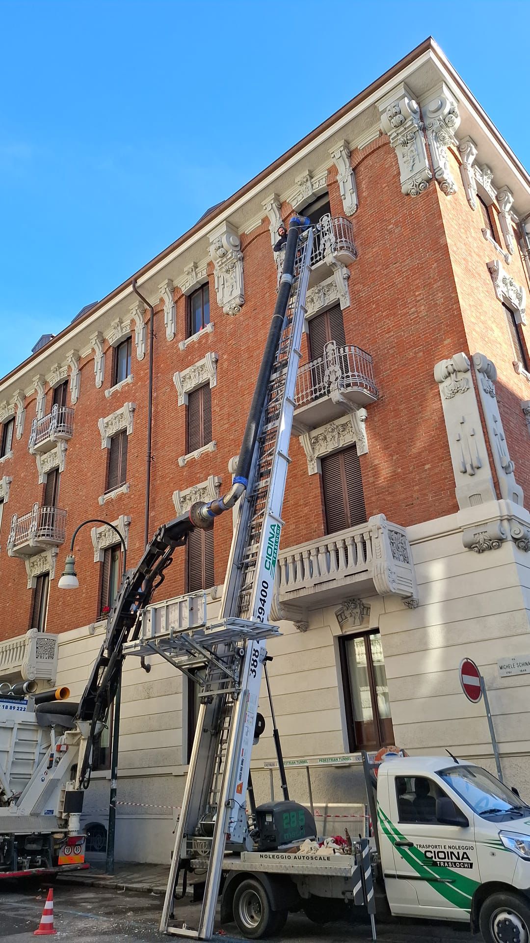Autoscala Cioina e autogru con braccio articolato al lavoro davanti a un palazzo liberty