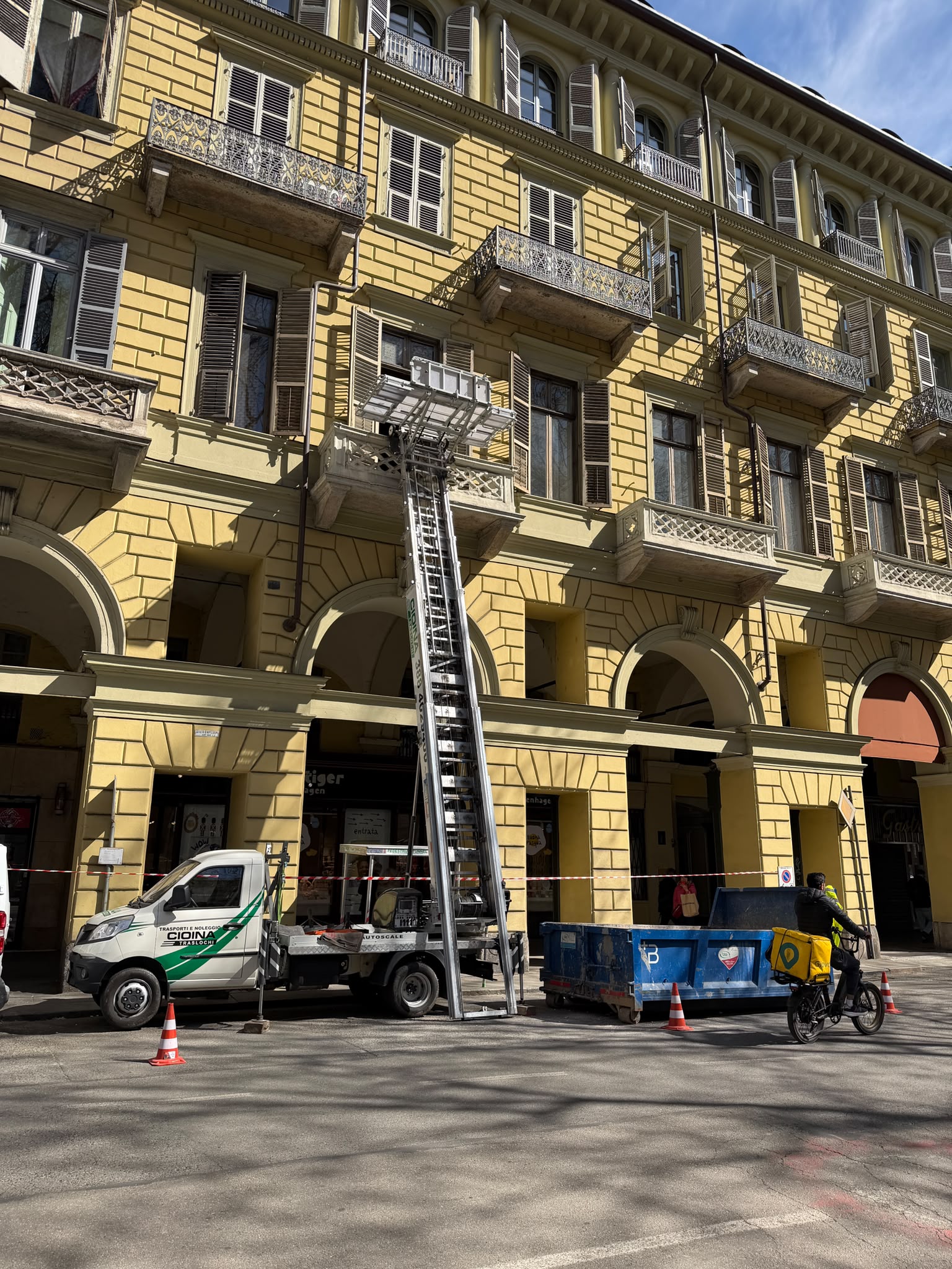 Trasloco con autoscala sotto i portici di un palazzo d'epoca torinese, area di lavoro delimitata da nastro e coni