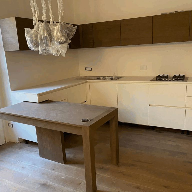 Cucina in legno e laccato chiaro appena montata, con il lampadario ancora protetto dalla pellicola